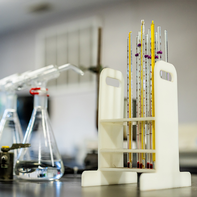 A fully equipped U.S. Sugar research laboratory with Erlenmeyer flasks, thermometer racks, reagent jugs, titration equipment and analytical instruments on a black lab bench, supporting science-backed cane sweetener development for agricultural applications