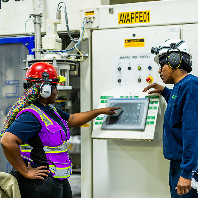 Two U.S. Sugar team members wearing hard hats and hearing protection review equipment controls while developing custom specialty cane sweetener solutions.