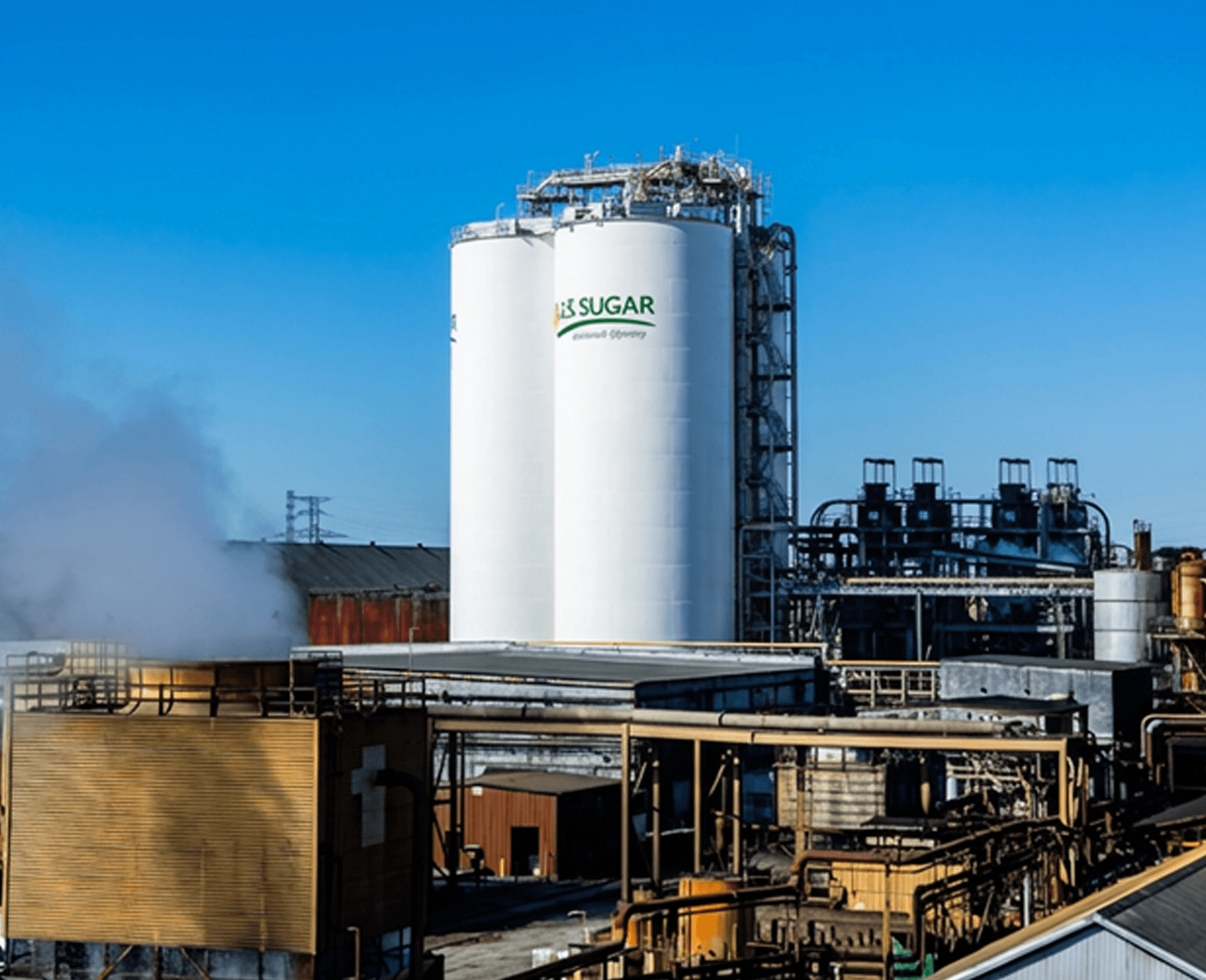 U.S. Sugar processing facility with large storage tanks and industrial infrastructure used in sugar refining operations.